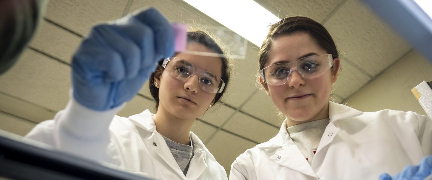 Two students in lab coats performing research in a lab